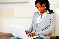 Portrait of an afro-American young female sitting at home on the floor using her laptop.