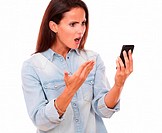 Portrait of angry adult female on blue blouse reading a message on her cell while screaming on isolated white bacckground.