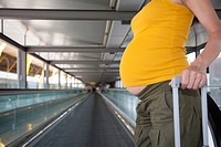 tummy of woman pregnant pulling suitcase in airport hall.