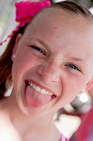 Portrait of a 10 year old girl with freckles sticking her tongue out at the camera making a funny face.