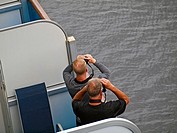 Two men with binoculars on a ships balcony.