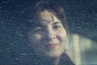 Young pretty woman smiling behind a spotted splashed car window