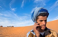 Morocco Sahara Desert sand dunes portrait of local man with turbin on cell phone in Las Palmeras area.