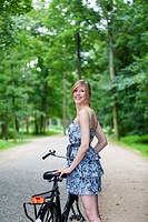 Happy blonde woman with bicycle in park smiling at camera