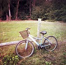 A bicycle sitting beside a barb wire fence in the countryside.