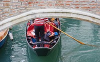 Gondolier in traditional red and white striped top rowing a gondola under a bridge, Castello, Venice, Veneto, Italy, Europe.