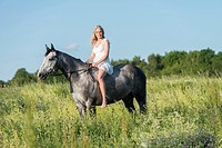 Girl in a white dress riding a grey horse.