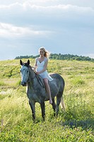 Barefoot girl in a white dress riding a grey horse.