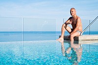 Man, 55 years old, hispanic ethnicity, sitting at upscale infinity swimming pool on the roof top of a condo building in Mexico.
