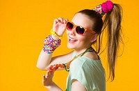 Smiling girl with colorful clothes wearing sunglasses, yellow background.