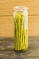 Preserved green asparagus in a glass on wooden table.