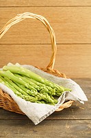Fresh green asparagus in a basket on wooden table.