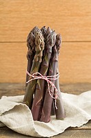 Bunch of fresh purple asparagus on wooden table with linen cloth.