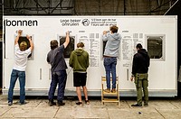 People removing a pricelist from the side of a portacabin at the end of a music festival (Ghent, Belgium). The sign reads ´Empty cup exchange´.
