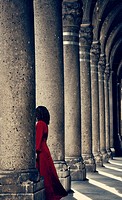 Mysterious woman in red dress behind column.