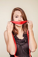 Young woman holding a red ribbon over her mouth.