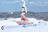 Young nude woman is laying with ski on snowpack with snow landscape background.