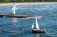 A sail boat passing the lighthouse at harbor in Swinoujscie, Poland.