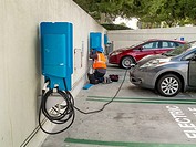 Repair technician maintaina an electric car charging station at an Irvine, CA, hospital parking lot. Note special parking slot notification in foregro...