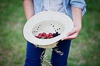Still life, girl taking a straw hat with berries inside.