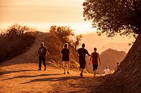 A small group of people walking on a hiking trail at sunset in the Hollywood Hills of Griffith Park, Los Angeles.