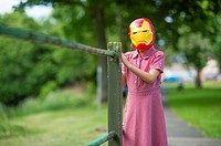 Childhood Games - young girl wearing an IronMan mask : Pre-teen primary school age children playing outdoors on a summer evening, dressed up as comic ...