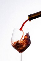 Vigorously wine poured from a bottle in a wine glass, on a white background.