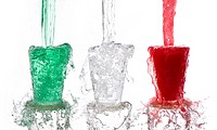 Tricolor drinks poured vigorously into three overflowing glasses on white background.