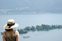 Woman with a straw hat watching Brissago islands and passenger ship on alpine lake Maggiore in Ticino, Switzerland.