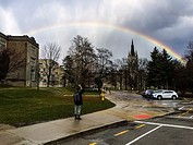 A young woman photographs a rainbow in an urban setting, Ontario, Canada