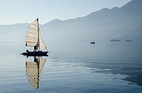 Sailing boat reflected on alpine lake Maggiore with Brissago islands and mountain in Ascona, Switzerland.