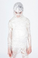 Little girl standing wrapped in transparent film like a mummy on a white background.