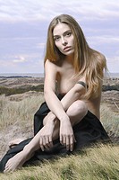 Nude woman portrait sitting on grass covered with black tissue. Combined image, natural dannish ladscape was taken as a backgroung.