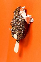 A chocolate bar isolotated on an orange background, drizled with toppings and more chocolate.