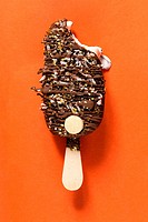 A chocolate bar isolotated on an orange background, drizled with toppings and more chocolate.