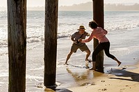Middle aged man and woman frolicking and chasing each other around boardwalk piers at the beach.