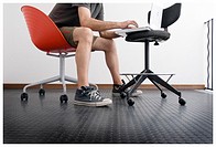 Adult man dressed casual with shorts sitting on an orange chair and handling a laptop on an office chair.