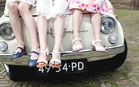 Helmond, Netherlands, 3 little girls with flowers all dressed up sitting on a vintage car