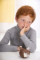 Little boy with red hair, head resting in one hand, thoughtful in front of an easter chocolate hen