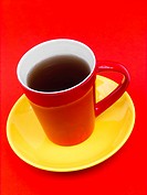 Coffee in red cup on yellow saucer against red background, colors representing spanish flag