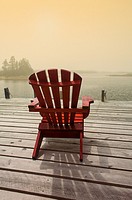 An Adirondack chair on a dock facing the Atlantic Ocean, Halifax, Canada. Warm, soft light provides a perfect time and place for meditation, mindfulne...