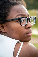 An African American teenager with black glasses is looking over her shoulders . Her white bra strap is showing. She looks thoughtful and sad.