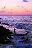 A lone fisherman casts his rod along Beirut's rocky Mediterranean shoreline at sunset, Lebanon.