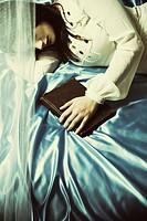 Sad young woman laying down in bed hand on book.