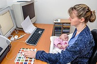 mother working at computer holding newborn baby.