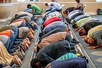 Muslim men prostrate themselves in ""Sujood"" prayer position with their faces on the Islamic patterned carpet at Friday afternoon prayers during reli...