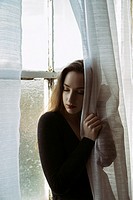 Sad young woman hands on the blinds by the window.