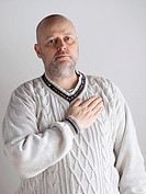 Portrait, casual looking caucasian male wearing a white pullover, right hand over heart and he looks toward the camera.