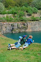 Three boys lie on the edge to a lake in an old stone pit in Bornholm, Denmark.
