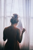 Rear view of a blond Caucasian woman standing by the window looking away.